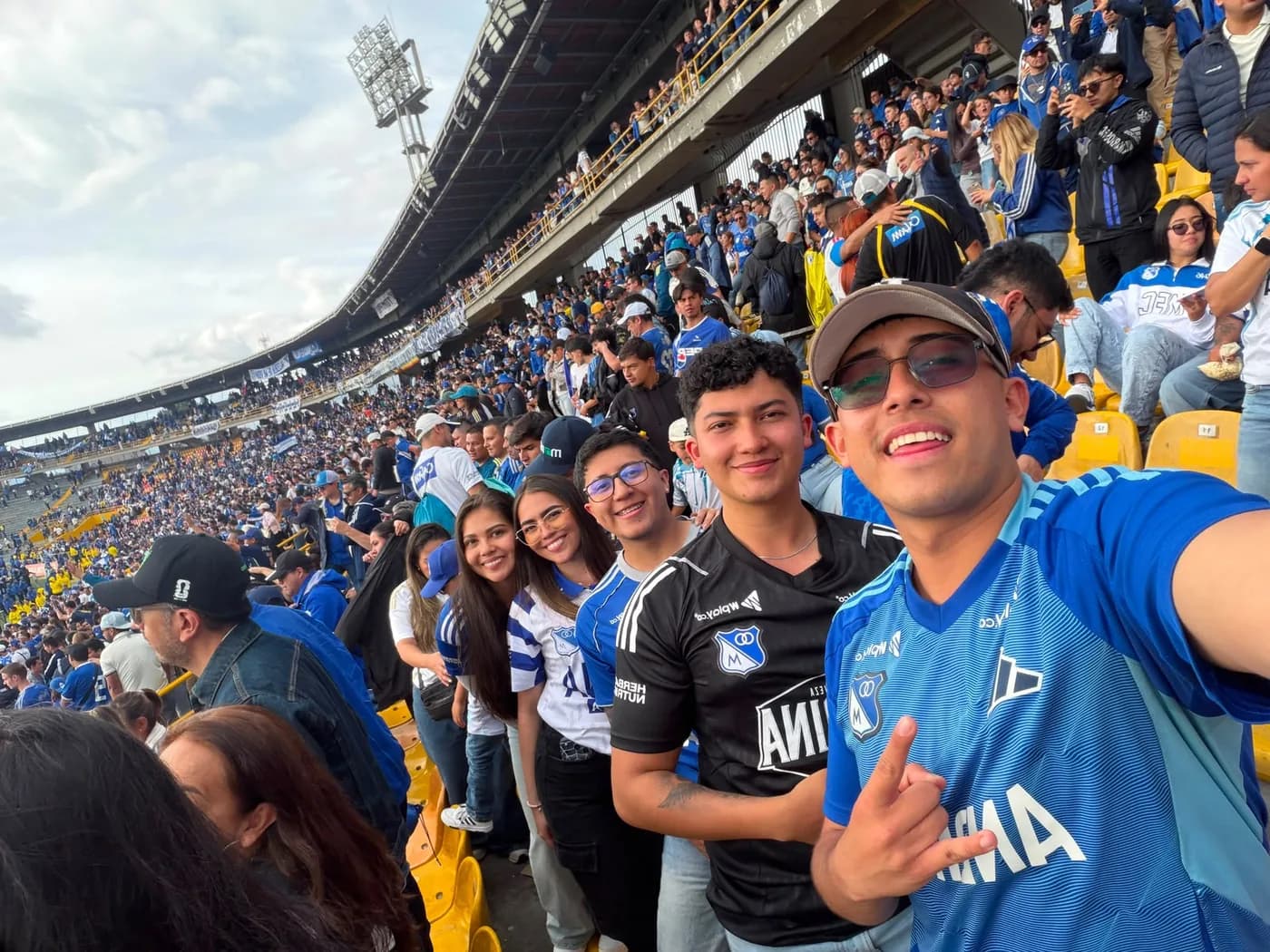 Grupo de amigos con camisetas de Millonarios en la tribuna llena de El Campín
